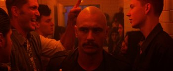 Movie still from “Zeroville” (2019), directed by James Franco – A man with a bald head and a crowd of people in the background; Close Up shot, Over the shoulder angle