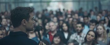 Movie still from “Zoe” (2018), directed by Drake Doremus – A crowd of people are gathered around a man holding a microphone; Close Up shot, Over the shoulder angle