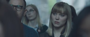 Movie still from “Zoe” (2018), directed by Drake Doremus – A woman in a black polka dot shirt is looking at the camera while two other women look on; Close Up shot, Over the shoulder angle