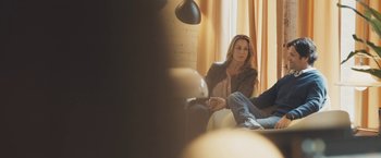Movie still from “Zoe” (2018), directed by Drake Doremus – A woman sitting on a couch in a room; Medium shot, Over the shoulder angle