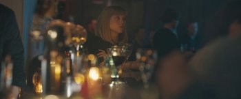 Movie still from “Zoe” (2018), directed by Drake Doremus – A woman sitting at a table holding a glass of wine; Close Up shot, Over the shoulder angle