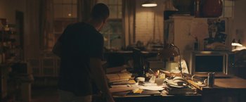 Movie still from “Zoe” (2018), directed by Drake Doremus – A man standing in front of a table with papers on top of it; Wide shot, High angle