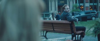 Movie still from “Zoe” (2018), directed by Drake Doremus – A man sitting on top of a wooden park bench; Medium shot, Over the shoulder angle