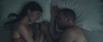 Movie still from “Zoe” (2018), directed by Drake Doremus – A man and a woman laying in a bed together; Medium shot, Overhead angle