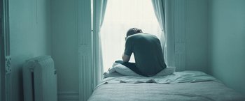 Movie still from “Zoe” (2018), directed by Drake Doremus – A man sitting on a bed looking out a window; Medium shot, High angle