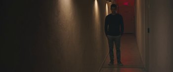 Movie still from “Zoe” (2018), directed by Drake Doremus – A man standing in a dark hallway with his hands in his pockets; Wide shot, Low angle