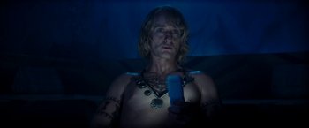 Movie still from “Zoolander 2” (2016), directed by Ben Stiller – A shirtless man holding a cell phone while sitting in a bed; Medium shot, High angle