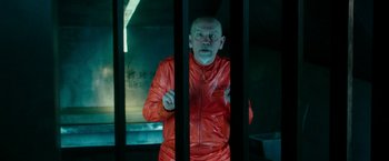 Movie still from “Zoolander 2” (2016), directed by Ben Stiller – A man in an orange jacket standing behind bars; Medium shot, Over the shoulder angle