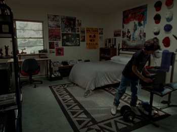 Movie still from “Mid90s” (2018), directed by Jonah Hill – A man standing in front of a bed in a room; Wide shot, High angle