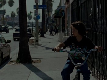 Movie still from “Mid90s” (2018), directed by Jonah Hill – A young man riding a bike down a street; Wide shot, High angle