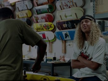 Movie still from “Mid90s” (2018), directed by Jonah Hill – A man standing in front of a wall of skateboards; Medium shot, Over the shoulder angle