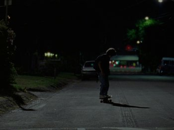 Movie still from “Mid90s” (2018), directed by Jonah Hill – A person riding a skate board on a city street at night; Wide shot, Low angle