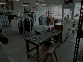 Movie still from “Mid90s” (2018), directed by Jonah Hill – A table in front of a clothing store with shirts hanging on the wall; Wide shot, High angle