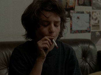 Movie still from “Mid90s” (2018), directed by Jonah Hill – A young boy sitting on a couch with a cigarette in his mouth; Close Up shot, Low angle