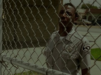 Movie still from “Mid90s” (2018), directed by Jonah Hill – A police officer standing in front of a chain link fence; Close Up shot, Low angle