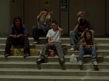 Movie still from “Mid90s” (2018), directed by Jonah Hill – A group of people sitting on some steps with skateboards; Wide shot, Low angle