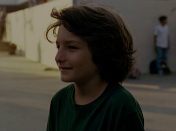 Movie still from “Mid90s” (2018), directed by Jonah Hill – A young boy with long brown hair wearing a green t - shirt; Close Up shot, Over the shoulder angle