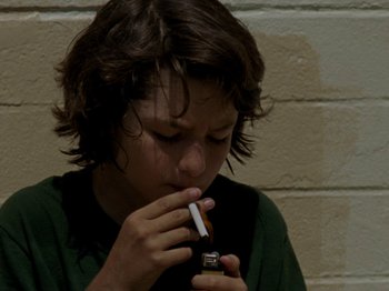 Movie still from “Mid90s” (2018), directed by Jonah Hill – A young boy is holding a cigarette in his mouth; Close Up shot, High angle