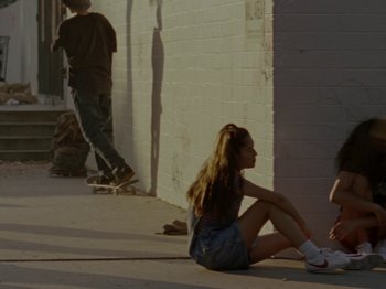 Movie still from “Mid90s” (2018), directed by Jonah Hill – A woman sitting on the ground next to a wall; Wide shot, High angle