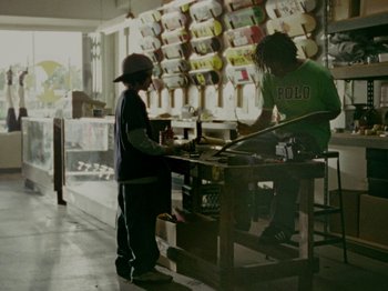 Movie still from “Mid90s” (2018), directed by Jonah Hill – Two people standing at a counter in a store; Wide shot, Low angle
