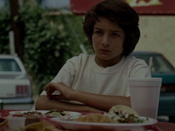 Movie still from “Mid90s” (2018), directed by Jonah Hill – A young boy sitting at a table with a plate of food in front of him; Close Up shot, Low angle