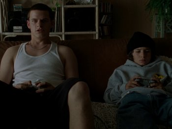 Movie still from “Mid90s” (2018), directed by Jonah Hill – A man sitting on a couch next to a young boy; Medium shot, High angle