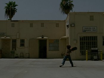 Movie still from “Mid90s” (2018), directed by Jonah Hill – A person is swinging a baseball bat in a parking lot; Extreme Wide shot, Low angle