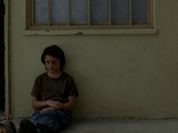 Movie still from “Mid90s” (2018), directed by Jonah Hill – A boy sitting on the ground in front of a window; Medium shot, High angle