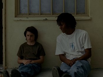 Movie still from “Mid90s” (2018), directed by Jonah Hill – Two people sitting on the ground in front of a window; Medium shot, High angle