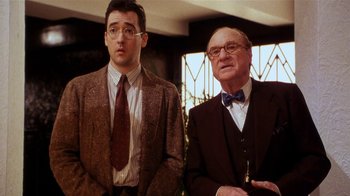 Movie still from “Bullets Over Broadway” (1994), directed by Woody Allen – A man and a man standing next to each other in a room; Medium shot, Over the shoulder angle