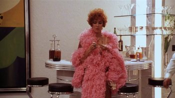 Movie still from “Bullets Over Broadway” (1994), directed by Woody Allen – A woman in a long pink coat standing next to a bar; Medium shot, High angle