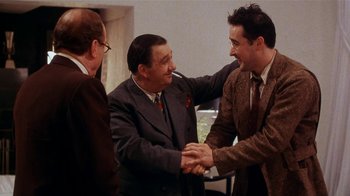 Movie still from “Bullets Over Broadway” (1994), directed by Woody Allen – A group of men shaking hands in a room; Medium shot, Over the shoulder angle
