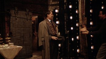 Movie still from “Bullets Over Broadway” (1994), directed by Woody Allen – A man in a suit and tie standing in front of lights; Wide shot, Over the shoulder angle
