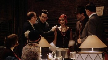 Movie still from “Bullets Over Broadway” (1994), directed by Woody Allen – A group of people standing around a table; Medium shot, Over the shoulder angle
