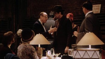 Movie still from “Bullets Over Broadway” (1994), directed by Woody Allen – A man in a suit and hat talking to another man in a suit and hat; Medium shot, Over the shoulder angle