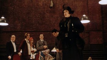 Movie still from “Bullets Over Broadway” (1994), directed by Woody Allen – A woman in a black outfit standing in front of a group of people; Medium shot, Over the shoulder angle