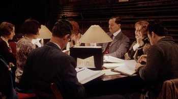 Movie still from “Bullets Over Broadway” (1994), directed by Woody Allen – A group of people sitting at a table with papers; Medium shot, High angle