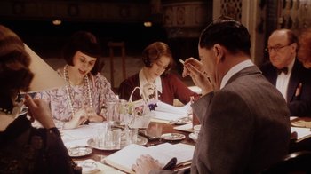 Movie still from “Bullets Over Broadway” (1994), directed by Woody Allen – A group of people sitting at a table with papers; Medium shot, High angle
