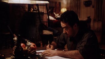Movie still from “Bullets Over Broadway” (1994), directed by Woody Allen – A man sitting at a table writing on a piece of paper; Medium shot, High angle