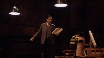 Movie still from “Bullets Over Broadway” (1994), directed by Woody Allen – A man in a suit and tie holding a book; Wide shot, Low angle