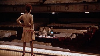 Movie still from “Bullets Over Broadway” (1994), directed by Woody Allen – A woman standing in front of two men in a theater; Wide shot, Low angle
