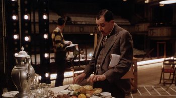 Movie still from “Bullets Over Broadway” (1994), directed by Woody Allen – A man standing at a table with food on top of it; Medium shot, Over the shoulder angle