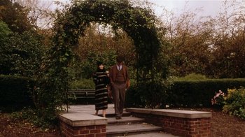 Movie still from “Bullets Over Broadway” (1994), directed by Woody Allen – A man and a woman walking under an archway in a park; Wide shot, High angle