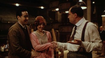 Movie still from “Bullets Over Broadway” (1994), directed by Woody Allen – Two men and a woman shaking hands in front of a building; Medium shot, Over the shoulder angle