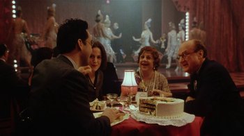 Movie still from “Bullets Over Broadway” (1994), directed by Woody Allen – A group of people sitting around a table with a cake; Medium shot, Over the shoulder angle