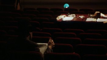 Movie still from “Bullets Over Broadway” (1994), directed by Woody Allen – A man sitting in a theater with a newspaper in his hand; Wide shot, High angle