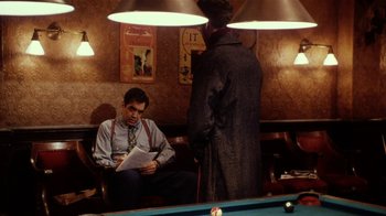 Movie still from “Bullets Over Broadway” (1994), directed by Woody Allen – A man sitting in front of a pool table; Medium shot, Over the shoulder angle