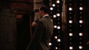 Movie still from “Bullets Over Broadway” (1994), directed by Woody Allen – A man wearing a suit and tie standing in front of a wall; Medium shot, Over the shoulder angle