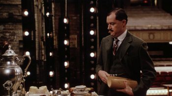Movie still from “Bullets Over Broadway” (1994), directed by Woody Allen – A man in a suit and tie holding a bag; Medium shot, Over the shoulder angle