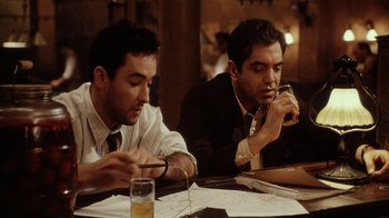 Movie still from “Bullets Over Broadway” (1994), directed by Woody Allen – A couple of men sitting at a table with papers; Medium shot, Low angle